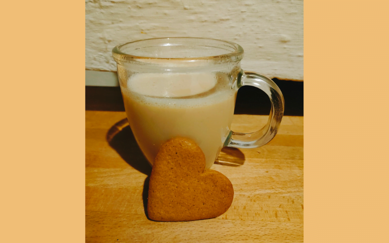 Comfort drankje Golden Milk in een doorzichtig theeglas met een koekje in de vorm van een hartje ervoor.